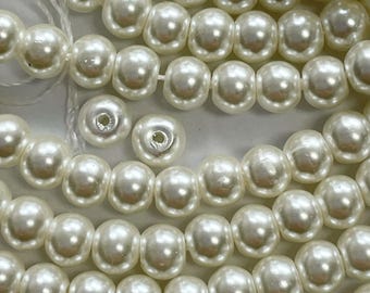 May include: A close-up of a strand of white pearl beads. The beads are round and smooth, and they have a slight iridescent sheen.