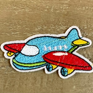 May include: A blue and red airplane embroidered patch with yellow accents. The airplane has a white window and a green outline.