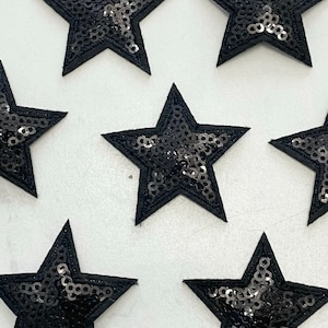 May include: Black star-shaped fabric patches with sequins. The patches are about 5 inches in diameter.