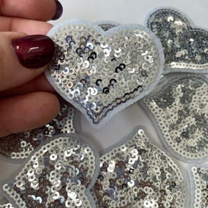 Könnte beinhalten: Ein Set silberner Pailletten-Aufnäher in verschiedenen Herz- und Kronenformen.