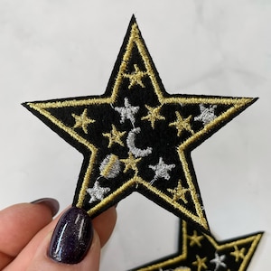 May include: A black felt star-shaped patch with gold and silver embroidered stars and crescent moons.