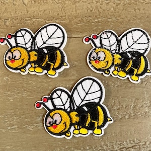 May include: Three embroidered iron-on patches of cartoon bees with black and yellow stripes, white wings, and red accents.
