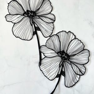 Puede incluir: Dos aplicaciones de flores de encaje negro con detalles delicados e intrincados. Las flores tienen un aspecto superpuesto y con volantes y están conectadas por un tallo delgado.