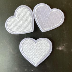 Puede incluir: Tres parches de fieltro blanco en forma de corazón. Los parches tienen un contorno blanco y están hechos de una tela suave y texturizada.