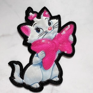May include: Embroidered patch featuring a white cartoon cat with a pink bow and a pink sequined bow. The cat has blue eyes, a pink nose, and black whiskers. The patch is outlined in black.
