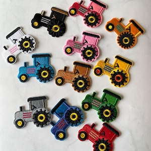 May include: A collection of colorful tractor patches in various shades, including pink, blue, and green. Each patch features a detailed design with black wheels and yellow accents. These embroidered patches are ideal for adding a touch of farm-themed flair to clothing or accessories.