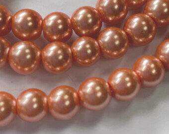 May include: A strand of peach-colored pearl beads. The beads are round and have a smooth, glossy finish.