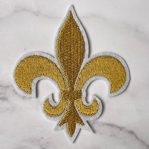 Op de afbeelding: Goud geborduurde fleur-de-lis patch met een witte omtrek.