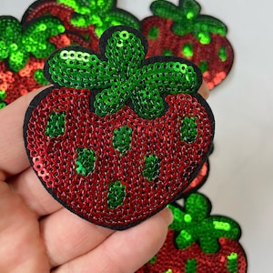 May include: A set of five red and green sequin strawberry patches. The strawberries are outlined in black and have a felt backing.
