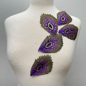May include: Five purple and gold peacock feather-shaped sequins with gold bead accents.