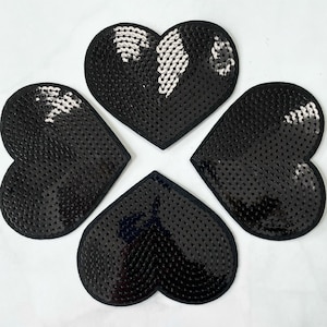 May include: Four black heart-shaped patches made of sequins. The sequins are arranged in a pattern that creates a textured look.
