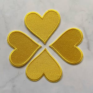 May include: Four yellow felt heart-shaped patches sewn together to form a clover shape.