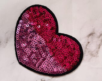 Puede incluir: Un parche en forma de corazón con borde negro, cubierto de lentejuelas rosas y fucsias. Las lentejuelas crean un efecto degradado, pasando del rosa claro a un fucsia vibrante. Este parche decorativo es ideal para añadir estilo a la ropa o accesorios.