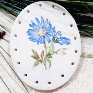May include: White ceramic oval dish with a blue and green floral design. The dish has holes around the edge.