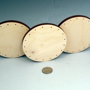 May include: Three round wooden discs with holes around the edge. The discs are different sizes and are arranged in a row. A US quarter is in the foreground for scale.