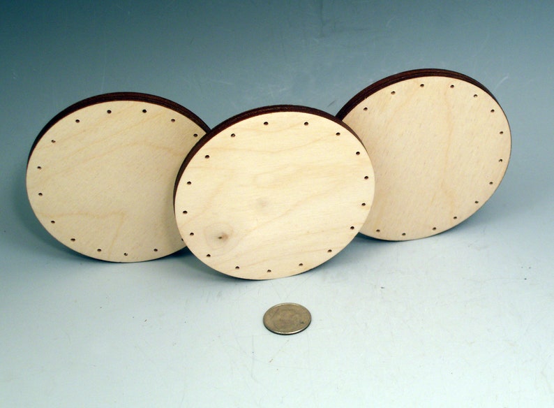 May include: Three round wooden discs with holes around the edge. The discs are different sizes and are arranged in a row. A US quarter is in the foreground for scale.