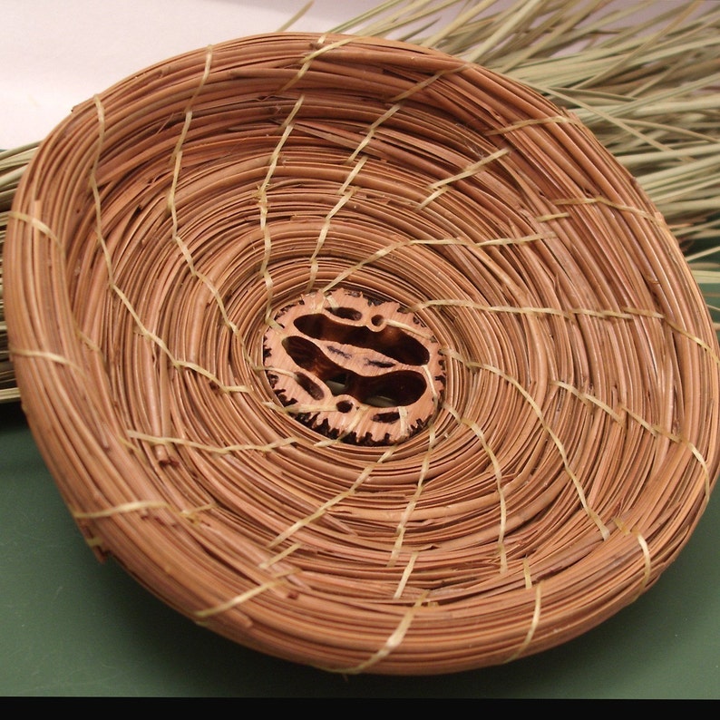 Peut inclure: Un panier tiss&eacute; en mat&eacute;riaux naturels, de forme circulaire et de couleur brune. Le panier a un &eacute;l&eacute;ment central d&eacute;coratif en bois.