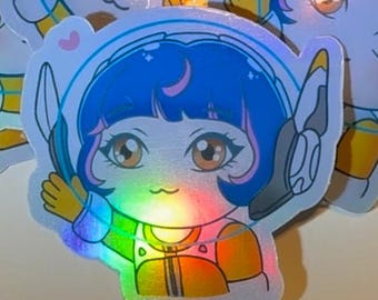 May include: Holographic sticker featuring a cartoon character with blue hair, a white helmet, and an orange and yellow jumpsuit. The character has large brown eyes and a small smile. The sticker has a rainbow sheen and is surrounded by other similar stickers.