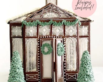 May include: A gingerbread house shaped like a greenhouse with dark brown walls, white icing details, and translucent windows. It features green icing garlands, two small green icing trees, and a pink circle with the text Recipes Included!