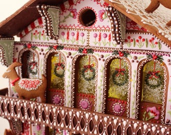 May include: A gingerbread house decorated with intricate details, including a white lace roof, red and white candy canes, and a pink and white floral design. Two gingerbread goats stand on the roof.