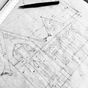 May include: Architectural blueprints with detailed sketches of a building's facade, including arched windows, decorative elements, and measurements. A black pen rests atop the drawing, alongside a ruler.