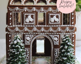 May include: A gingerbread house featuring white icing details, arched windows, and a central entryway. Two green icing trees with white sugar dusting sit in front. A pink circular sticker on the upper right displays the text Recipes Included!