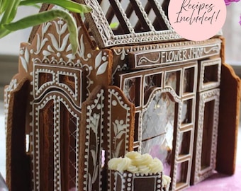 May include: A gingerbread house shaped like a flower shop with white icing details, a roof with open lattice panels, and a sign reading FLOWER SHOP. A pink circular sticker on the roof says Recipes Included! A small rectangular planter sits in front.