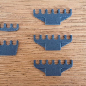 May include: Four grey plastic combs of varying sizes, arranged on a wooden surface.