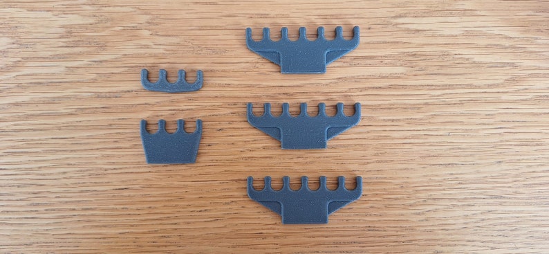 May include: Four grey plastic combs of varying sizes, arranged on a wooden surface.