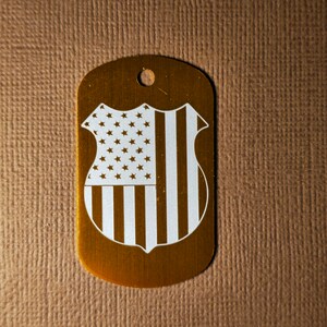 May include: Gold-colored metal dog tag with a white American flag design.
