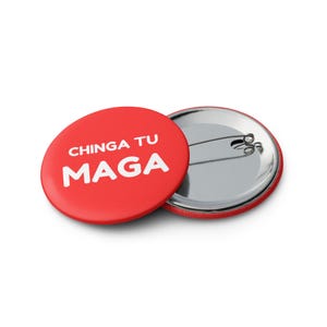 May include: Red button with white text that reads "CHINGA TU MAGA". The back of the button is silver.