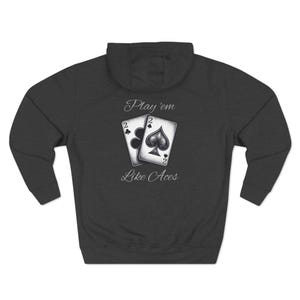 May include: Dark gray hoodie featuring a graphic of two playing cards, the two of clubs and the two of spades. The text "Play 'em Like Aces" is printed above and below the cards in a script font. The hoodie has a hood and long sleeves.