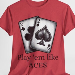 May include: Red t-shirt featuring a graphic of two playing cards, the two of clubs and the two of spades. The text "Play 'em like ACES" is printed below the cards in a dark color.