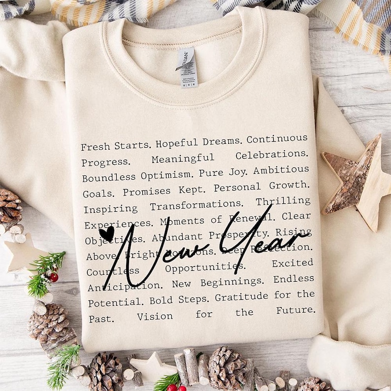 Op de afbeelding: Een beige sweatshirt met een zwart tekstontwerp dat luidt "Fresh Starts. Hopeful Dreams. Continuous Progress. Meaningful Celebrations. Boundless Optimism. Pure Joy. Ambitious Goals. Promises Kept. Personal Growth. Inspiring Transformations. Thrilling Experiences. Moments of Renewal. Clear Objectives. Abundant Prosperity. Rising Above Fright. New Year. Countless Opportunities. Excited Anticipation. New Beginnings. Endless Potential. Bold Steps. Gratitude for the Past. Vision for the Future."