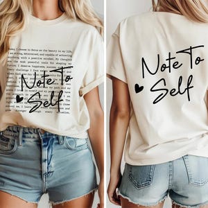 May include: White t-shirt with short sleeves and a black print on the front that says "Note To Self" and a black heart. The back of the shirt has a black print that says "Note To Self" with a black heart.