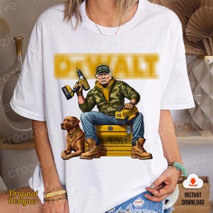 Puede incluir: Una camiseta blanca con un gráfico de un hombre con camuflaje sosteniendo un taladro y una caja de herramientas. El texto "DWALT" está impreso en amarillo sobre el gráfico. El hombre lleva una gorra roja "Make America Great Again".