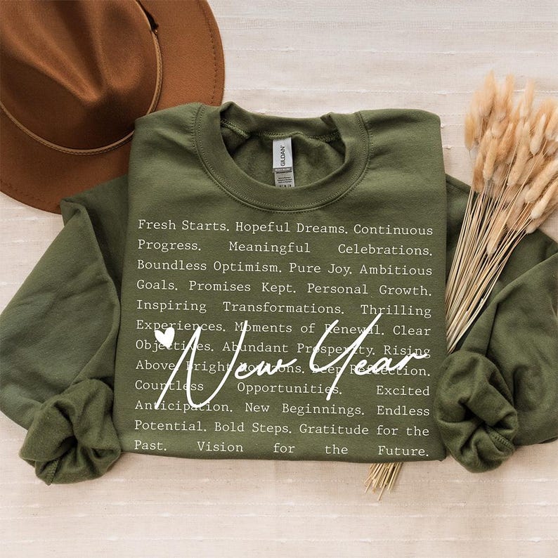 Op de afbeelding: Een groen sweatshirt met witte tekst die luidt: "Fresh Starts. Hopeful Dreams. Continuous Progress. Meaningful Celebrations. Boundless Optimism. Pure Joy. Ambitious Goals. Promises Kept. Personal Growth. Inspiring Transformations. Thrilling Experiences. Moments of Renewal. Clear Objectives. Abundant Prosperity. Rising Above. New Year. Countless Opportunities. Anticipation. New Beginnings. Endless Potential. Bold Steps. Gratitude for the Past. Vision for the Future."