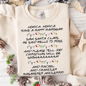Puede incluir: Una sudadera beige con un diseño navideño de Friends. El texto dice "Monica, Monica. Have a Happy Hanukkah. Saw Santa Claus. He said hello to Ross. And please tell Joey Christmas will be snowaaaaay. And Rachel and Chandler Hasaherer Andlerrr!"