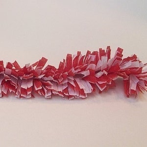 May include: Red and white paper streamer garland. The garland is made of thin strips of paper that are curled and twisted to create a fluffy, festive look.