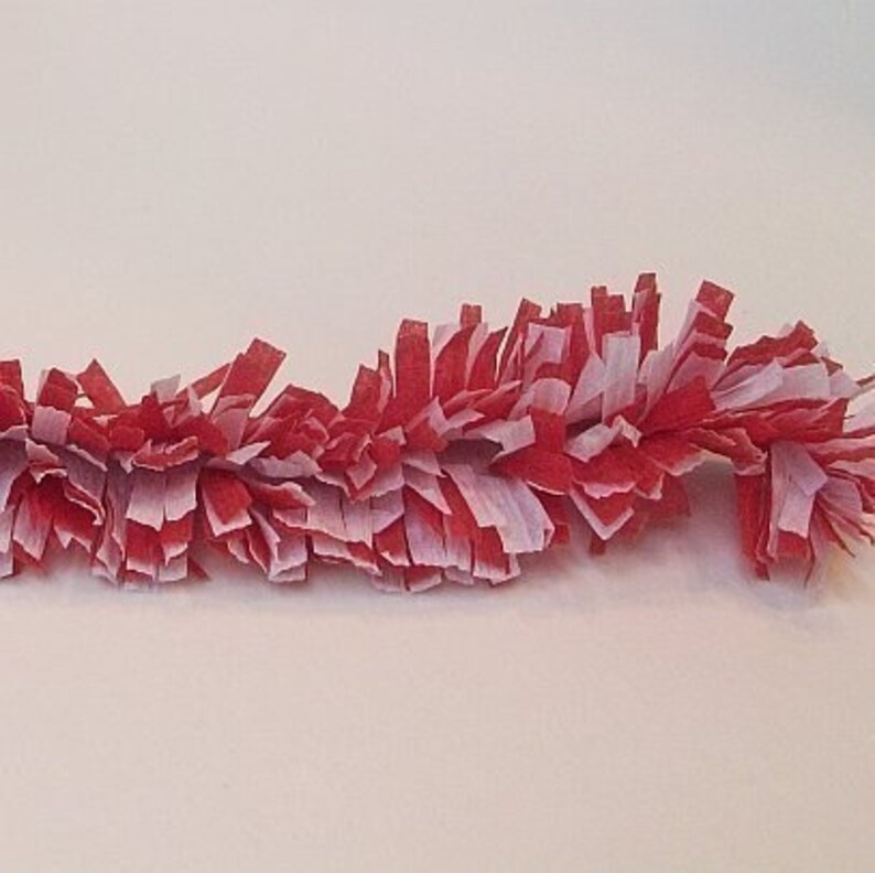 May include: Red and white paper streamer garland. The garland is made of thin strips of paper that are curled and twisted to create a fluffy, festive look.