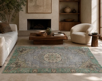 May include: A rectangular area rug featuring a central floral medallion in cream and sage green, surrounded by a grey field and a wide border with intricate botanical patterns in shades of teal, brown, and cream on a distressed, vintage-style base.