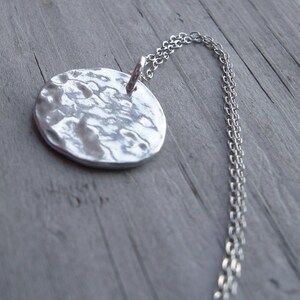 Può includere: Una collana d'argento con un ciondolo rotondo martellato. La catena è di stile delicato e a maglie.