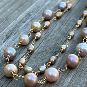 May include: Close-up of two strands of pearl necklaces. The pearls vary in size and color, ranging from light pink to gold and gray. The pearls are strung on delicate gold chains, creating an elegant and timeless look.