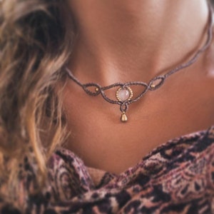 Op de afbeelding: Een delicate ketting van bruin koord met een geknoopt ontwerp en een enkele roze edelsteen hanger.