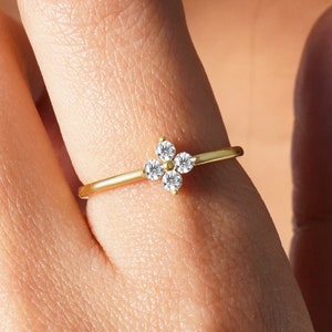 Può includere: Un delicato anello in oro con una piccola montatura a quattro griffe che presenta un gruppo di pietre rotonde trasparenti.