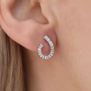May include: A pair of silver hoop earrings with a curved design. The earrings are set with small, baguette-shaped diamonds.