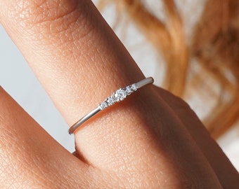 Puede incluir: Un delicado anillo de plata con una fila de pequeños diamantes transparentes engastados en una banda curva.