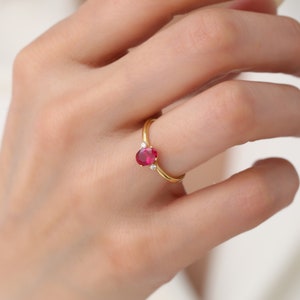 May include: A gold ring with a red oval gemstone and two smaller white gemstones on the band.