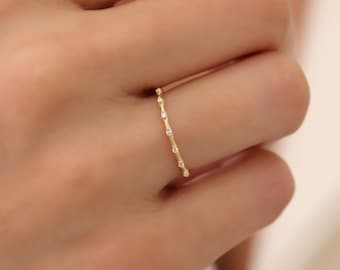 May include: A delicate gold ring with a row of small, clear gemstones set in a simple, minimalist design.