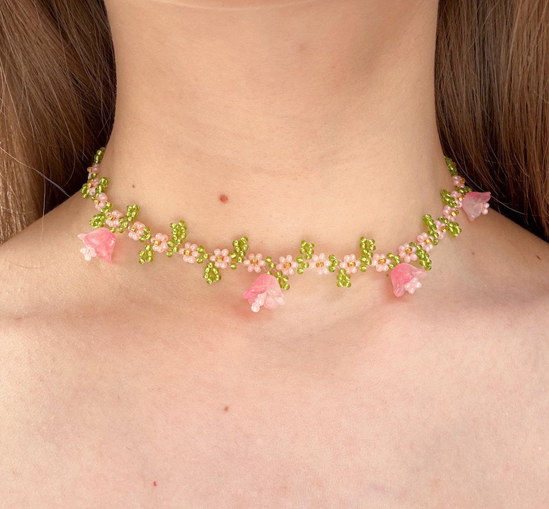 May include: A delicate choker necklace made with pink and green beads, featuring a floral design with small pink flowers and larger pink flower accents.